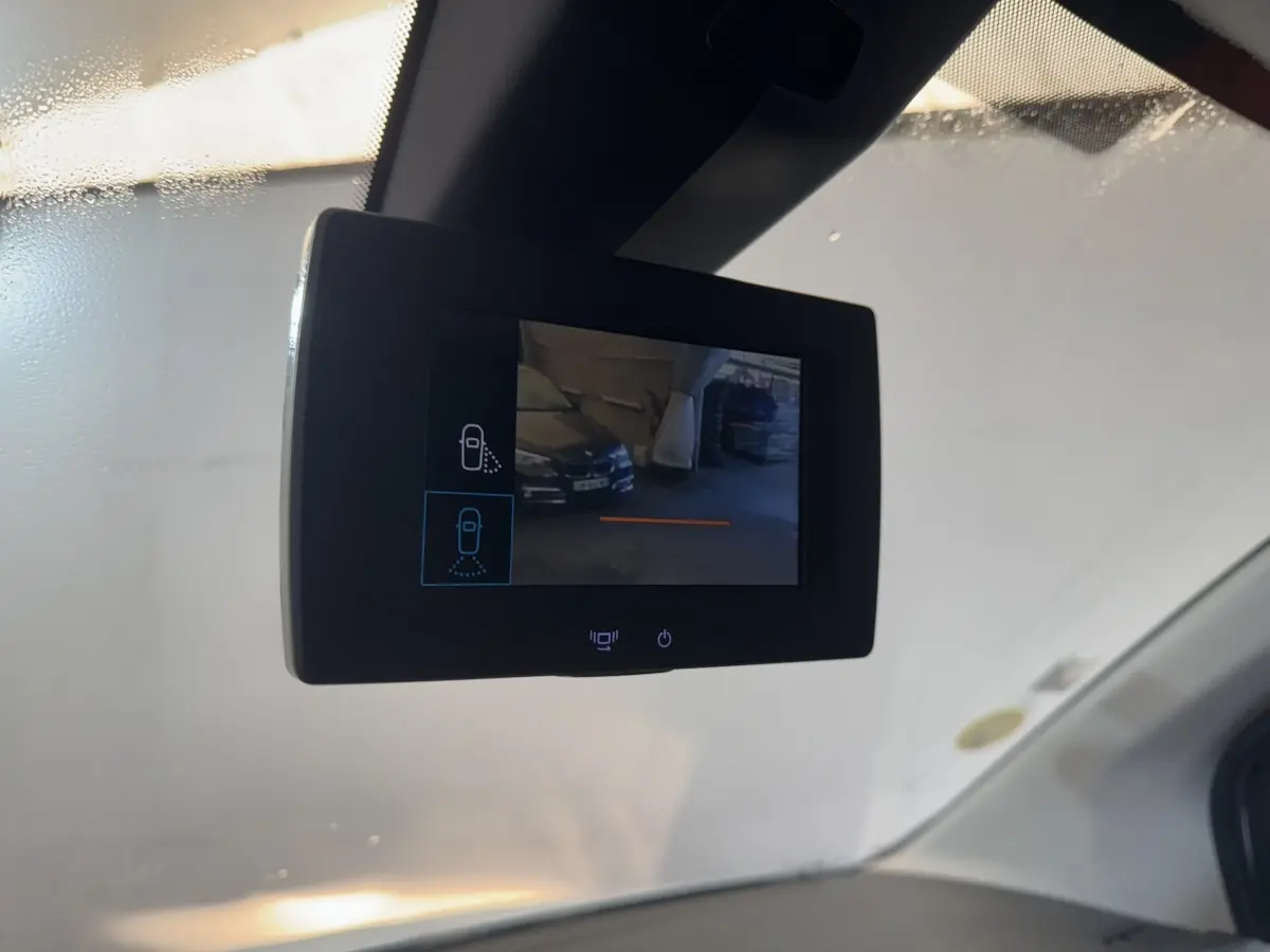 Écran de rétroviseur caméra intérieur affichant une vue arrière partielle d’un véhicule noir en parking.