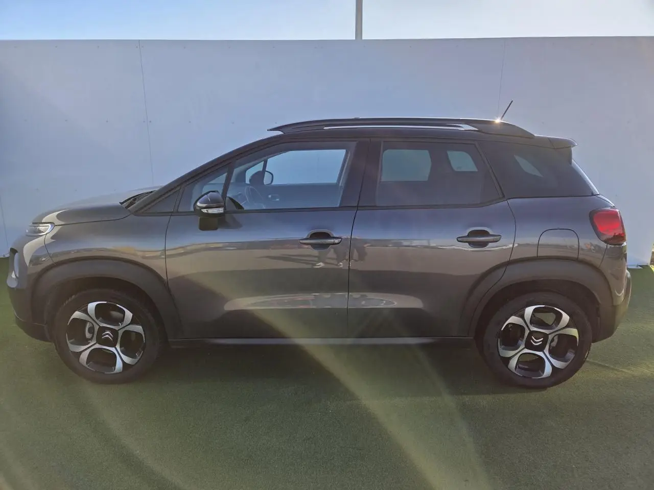 Vue de face d'un Citroën C3 Aircross gris platinium avec toit noir perlé et barres de toit argentées sur fond urbain.