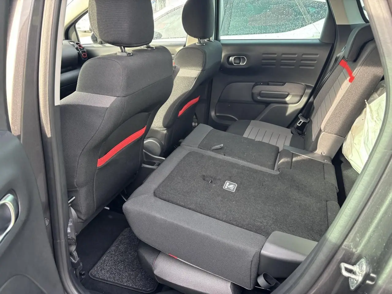 Vue intérieure arrière droite du Citroën C3 Aircross gris, banquette arrière rabattue avec détails rouges sur sièges avant.
