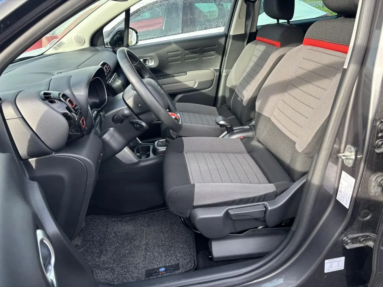 Vue intérieure côté conducteur du Citroën C3 Aircross 2021, sièges tissu gris avec bande rouge et tableau de bord noir.