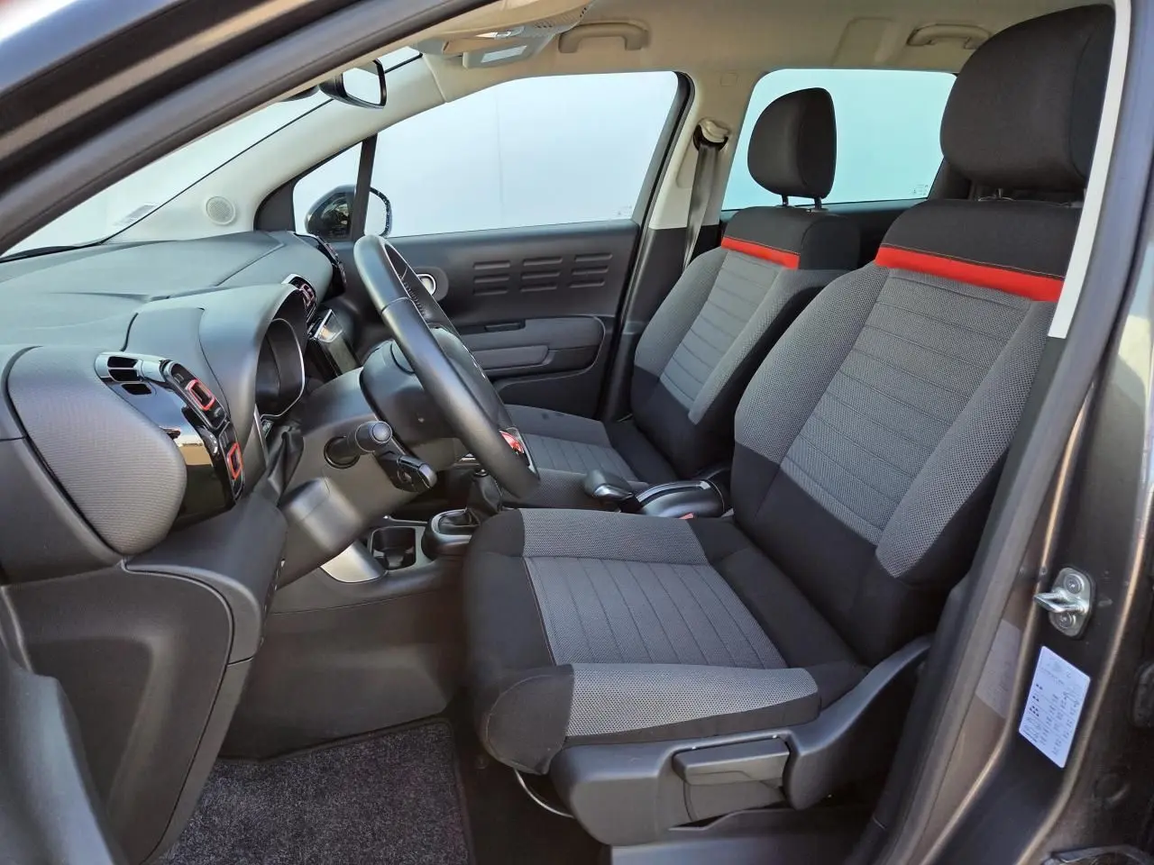 Intérieur avant droit de Citroën C3 Aircross gris platinium, sièges tissu gris avec bande rouge et tableau de bord noir brillant.