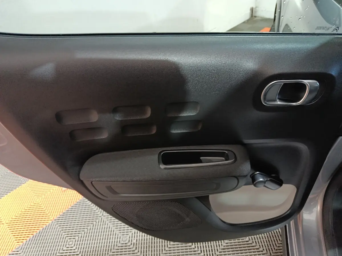 Vue rapprochée de la porte côté gauche intérieure d'une Citroën C3 gris foncé avec poignée chromée et manivelle de vitre.