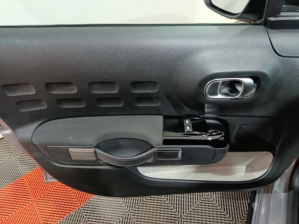 Gros plan sur la porte côté conducteur de la Citroën C3 gris foncé, avec poignée noire et commandes de vitres intégrées.