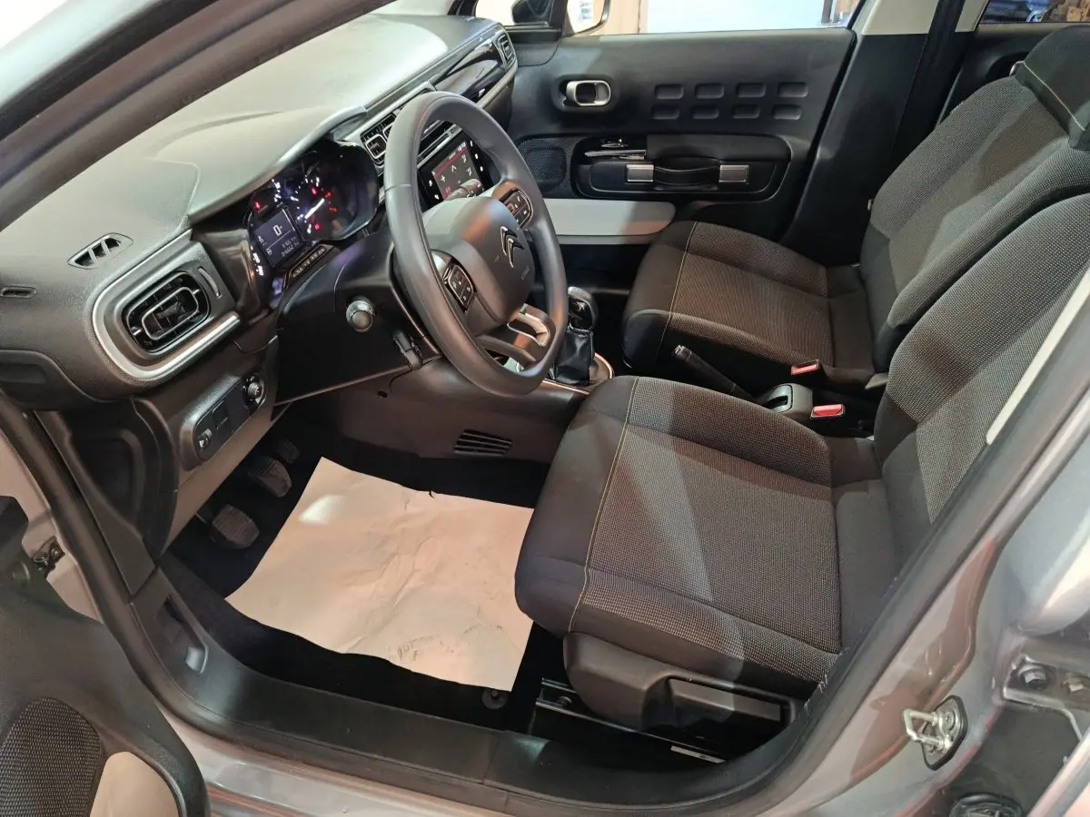 Intérieur côté conducteur de la Citroën C3 gris foncé 2024, avec tableau de bord moderne et sièges en tissu noir.