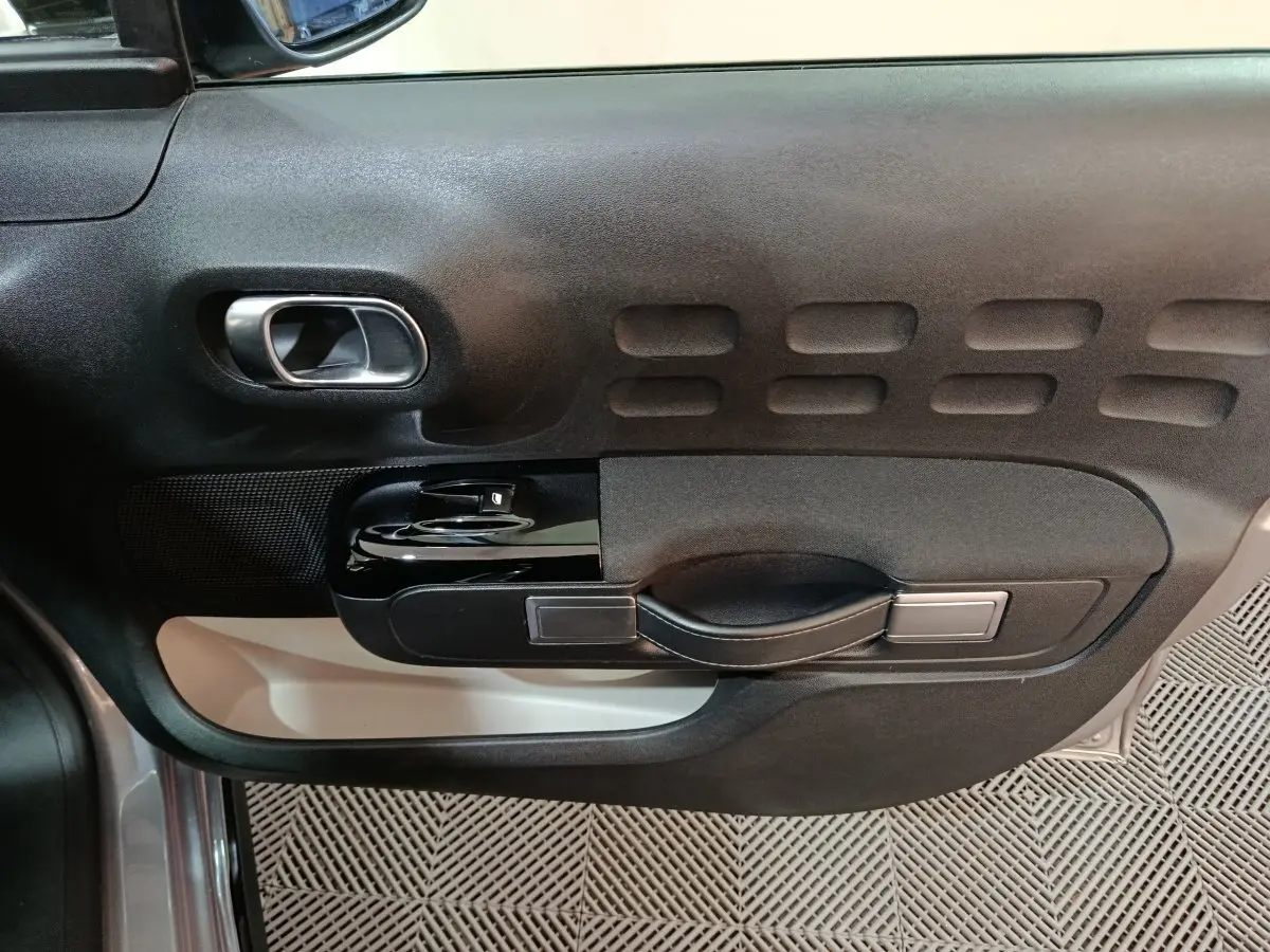 Gros plan sur la porte côté gauche de la Citroën C3 gris foncé, montrant la poignée et les commandes de vitre.