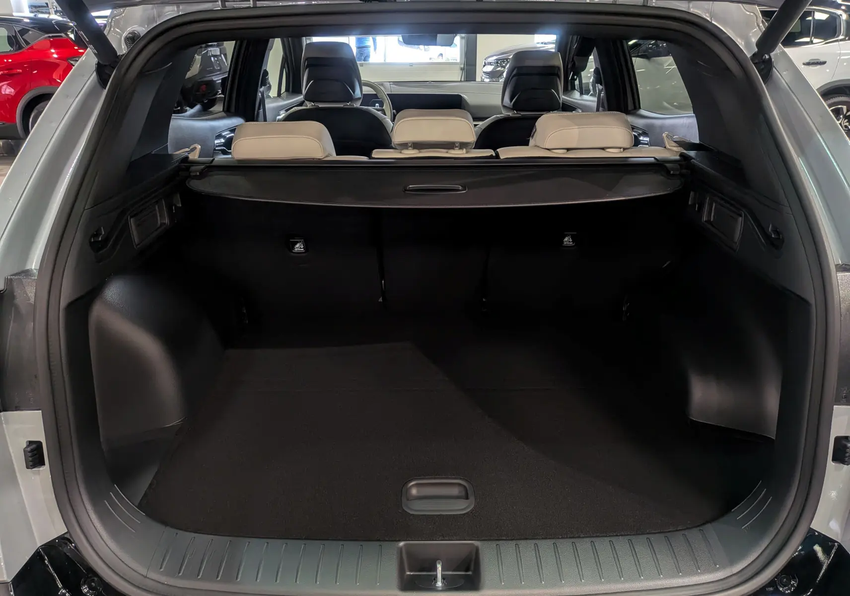 Coffre ouvert du Kia Sportage 2025 gris céramique avec intérieur noir et sièges arrière beiges visibles.