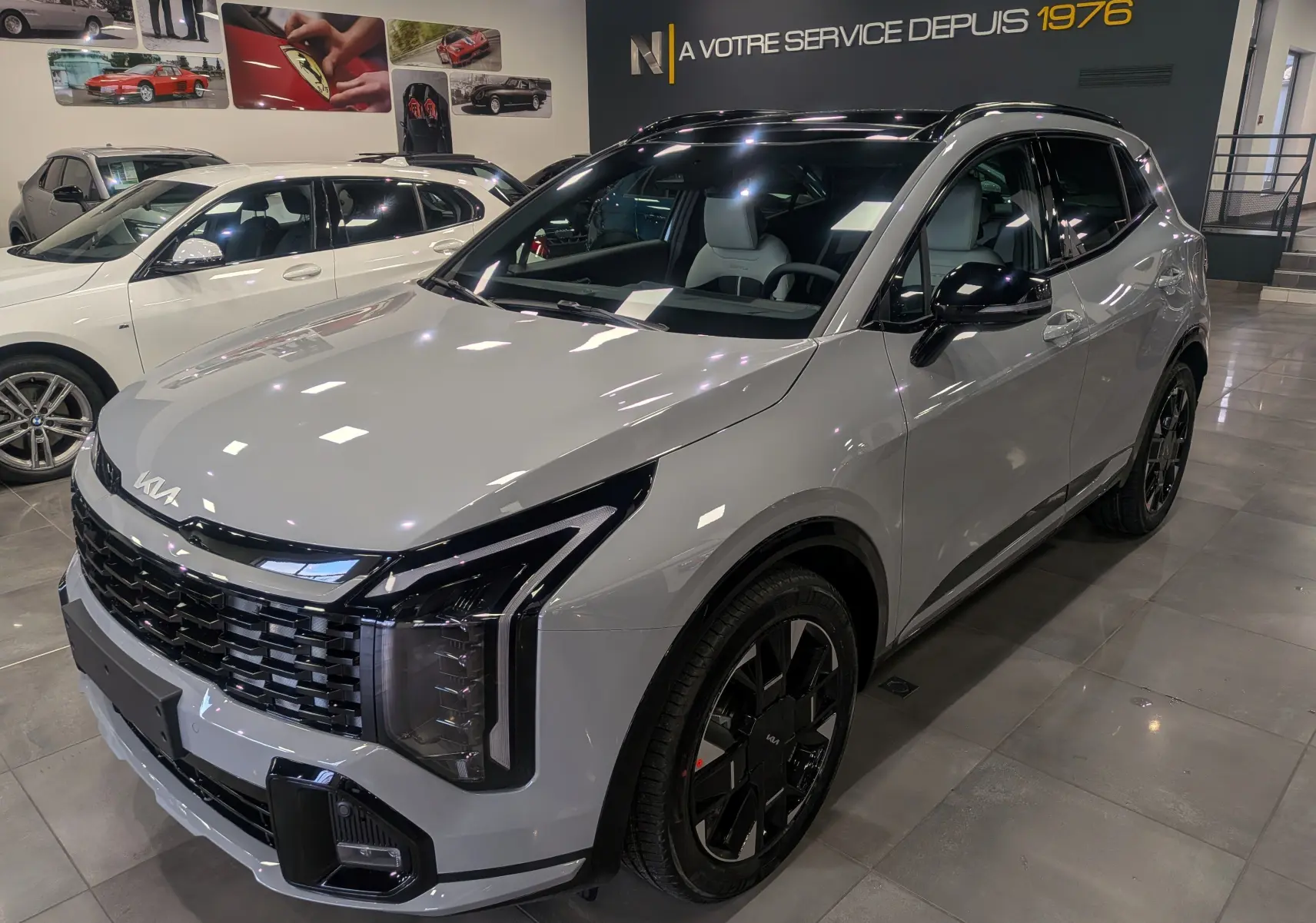KIA SPORTAGE gris céramique avec toit noir, vue 3/4 avant droit en intérieur de showroom.