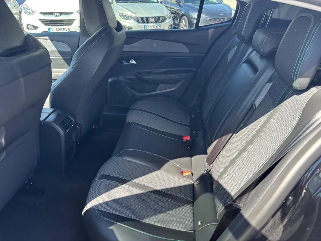 Vue latérale droite des sièges arrière noirs en cuir et tissu du Peugeot 408 Hybrid 2025 avec ceinture de sécurité et accoudoir central.