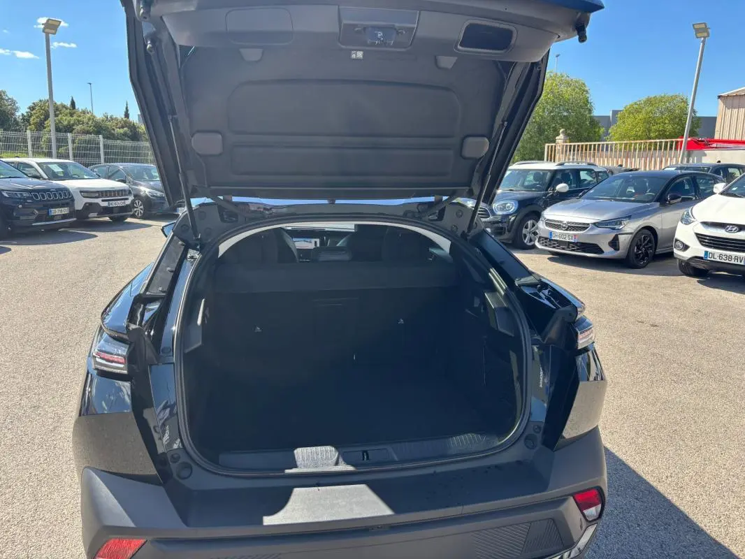 Coffre ouvert vu de l'arrière d'une Peugeot 408 Hybrid 136 e-DCS6 Allure noire, avec hayon relevé en extérieur.