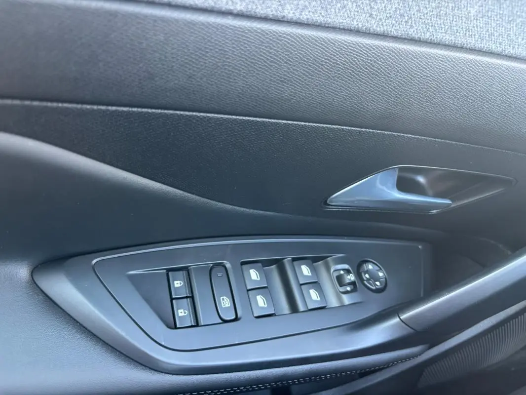 Gros plan sur la commande des vitres et rétroviseurs côté conducteur de la Peugeot 408 Hybrid noire, finition Allure 2025.