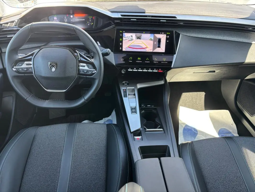 Vue intérieure avant de la Peugeot 408 Hybrid noire, avec volant compact, écran tactile central et cockpit numérique.