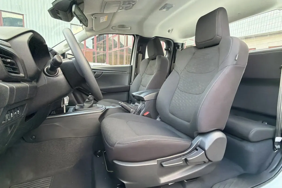 Vue intérieure côté conducteur de l'Isuzu D-MAX 2026, sièges tissu gris avec accoudoir central et volant multifonctions.