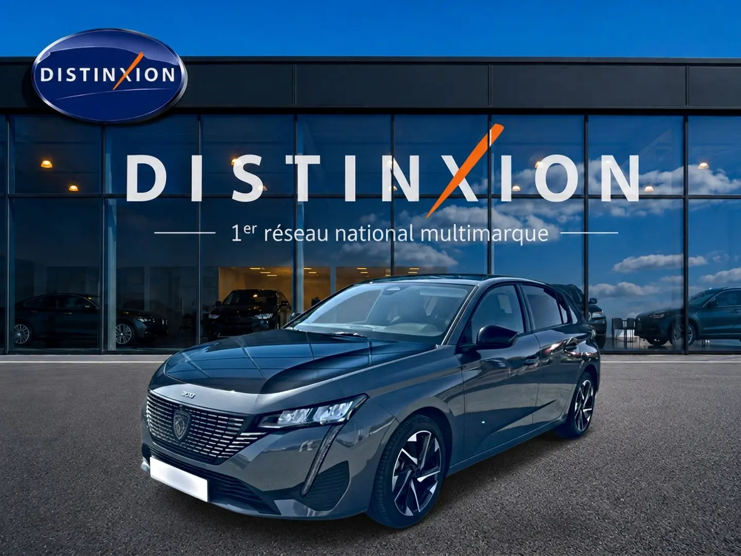 Peugeot 308 gris 3/4 avant droit, jantes alu noires, devant vitrine Distinxion avec reflet ciel bleu.