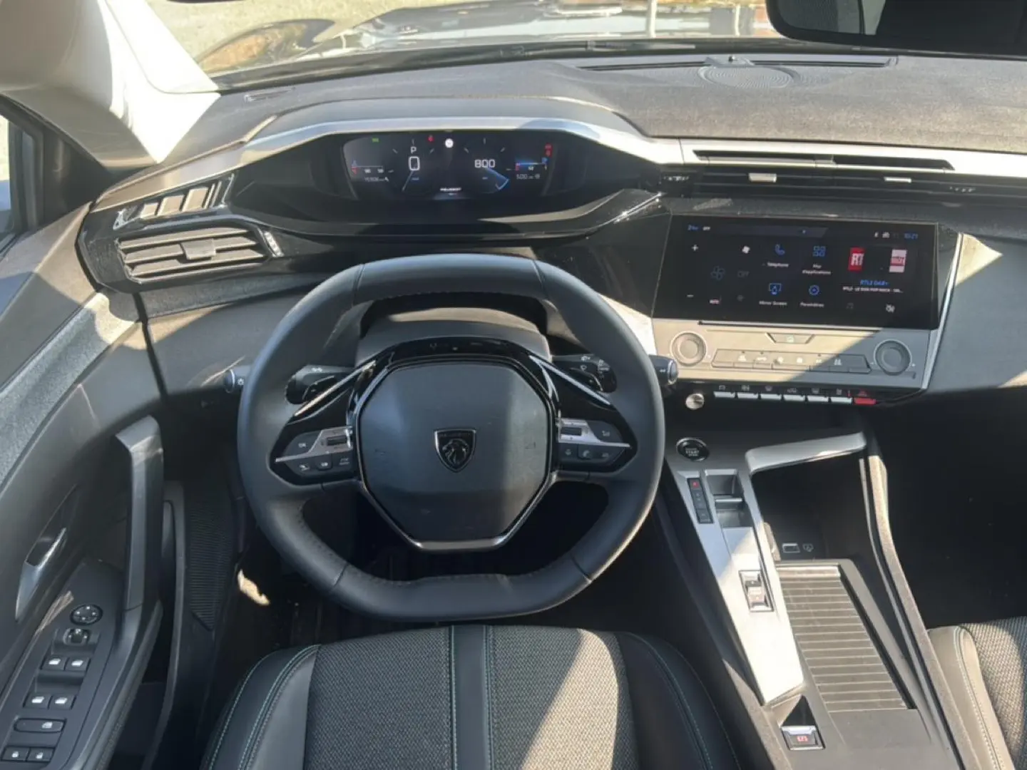 Vue intérieure frontale du poste de conduite gris de la Peugeot 308 2025 avec volant multifonction et écran tactile central.