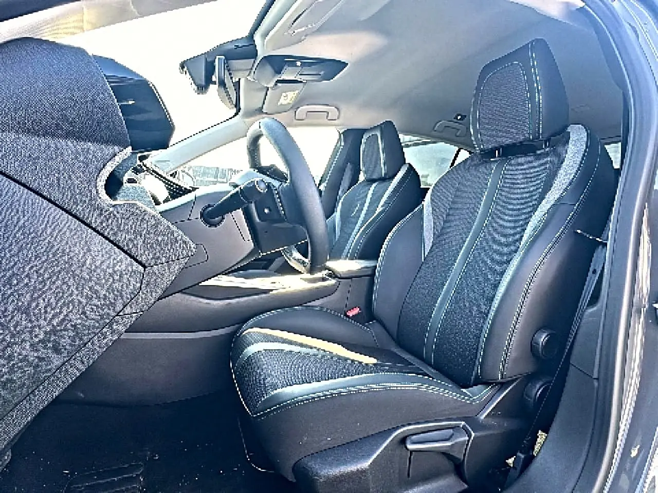 Vue intérieure côté conducteur de la Peugeot 308 2025, sièges tissu noir avec surpiqûres contrastées et volant multifonction.