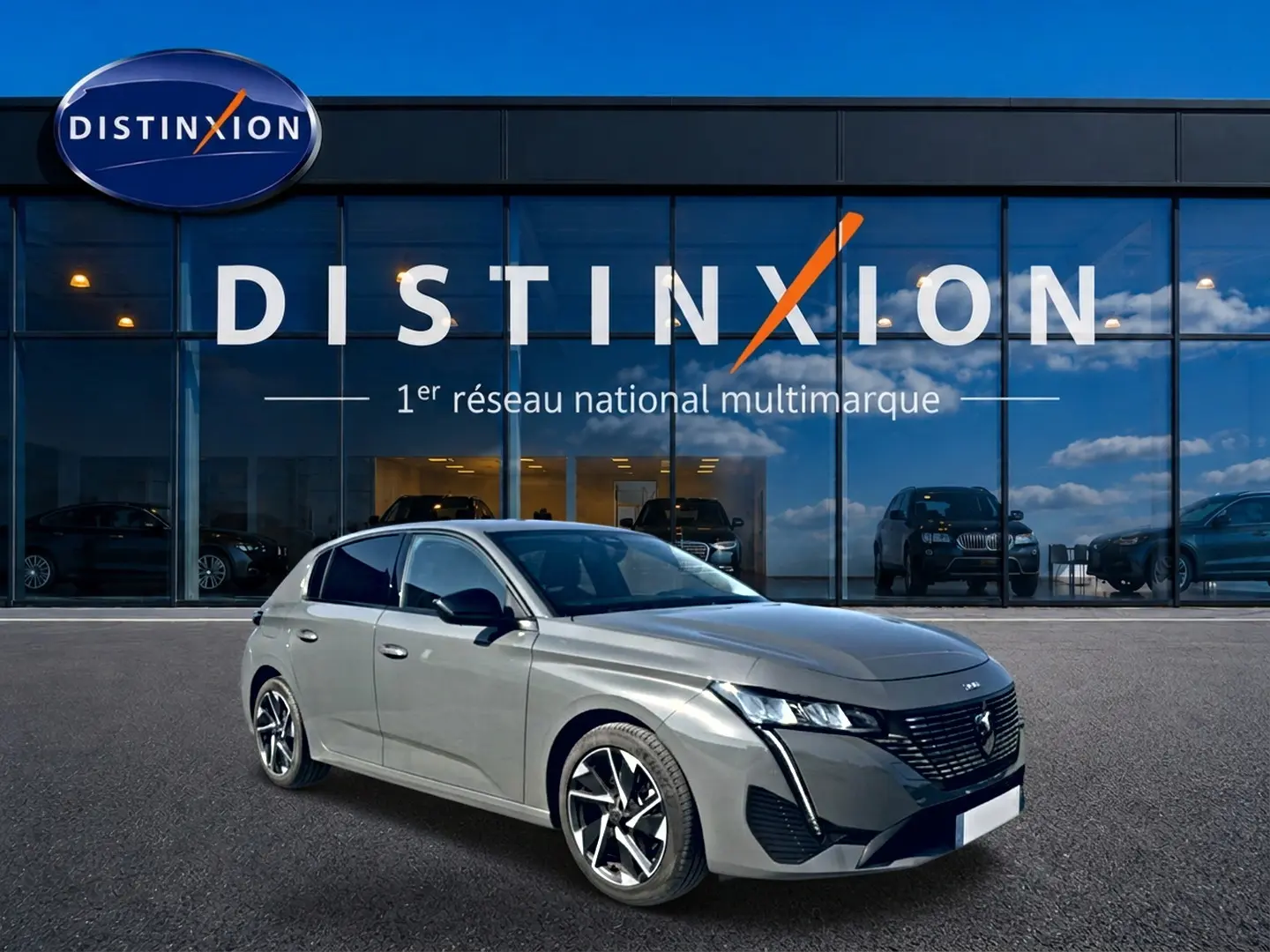 Peugeot 308 gris en 3/4 avant droit, avec jantes alu et calandre distinctive, devant une vitrine Distinxion.