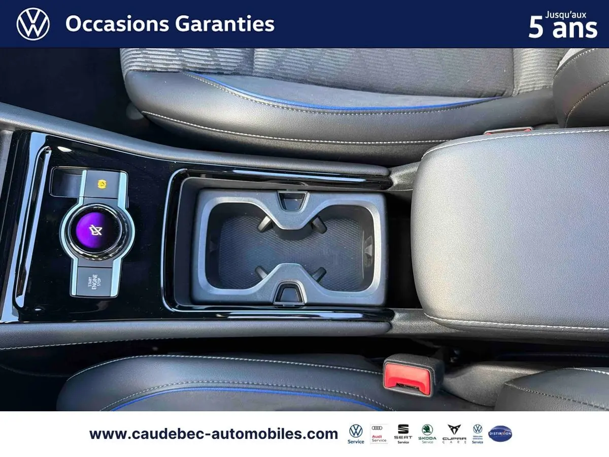 Vue plongeante sur la console centrale noire brillante du Volkswagen Tiguan eHybrid avec porte-gobelets et accoudoir gris.