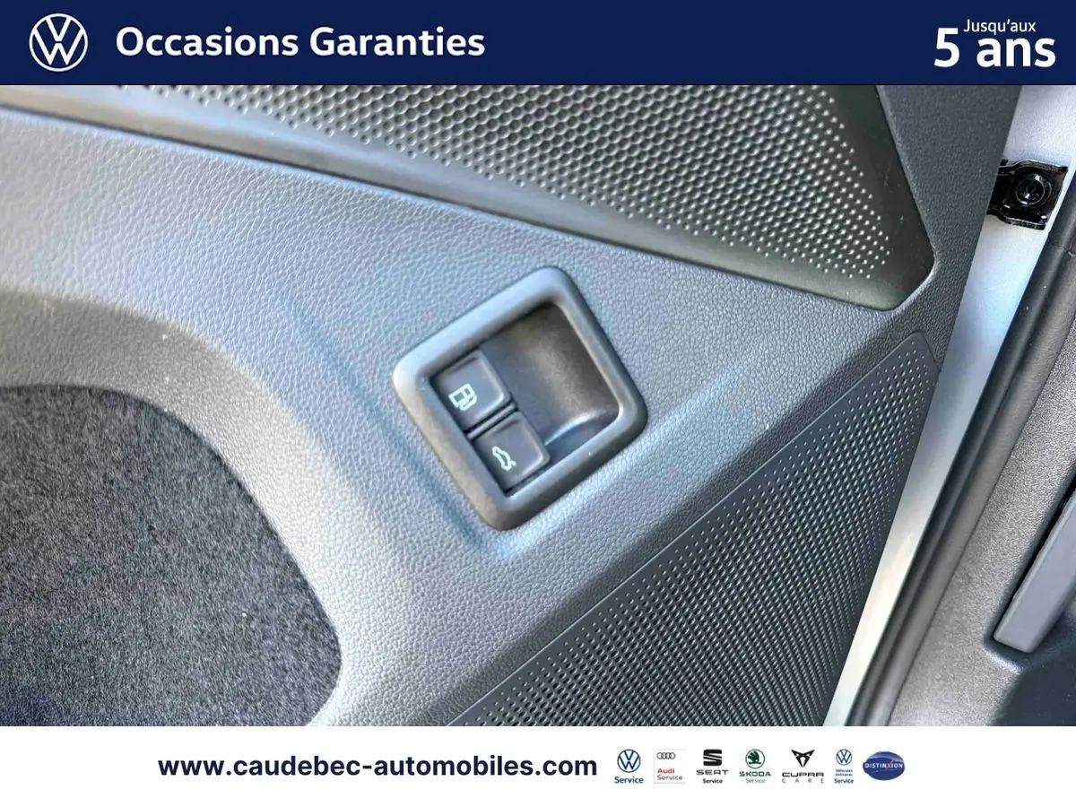 Gros plan sur la commande d'ouverture du hayon et du bouchon de carburant sur la porte intérieure d'un Volkswagen Tiguan argent Dolomite.