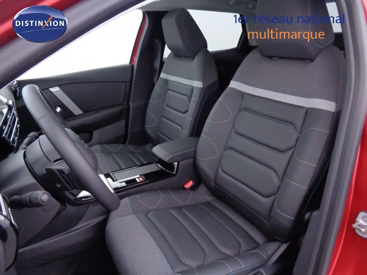 Vue intérieure côté conducteur de la Citroën C4 X rouge Elixir, sièges noirs en cuir et tissu avec console centrale visible.