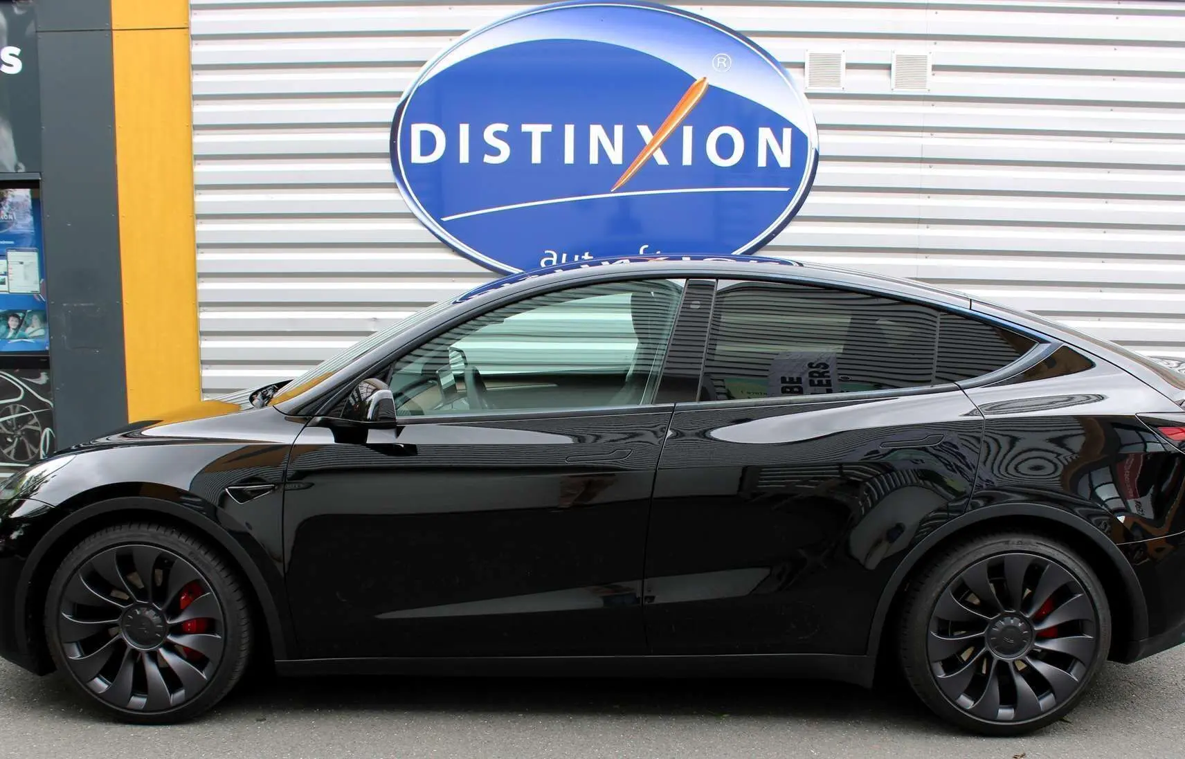 Profil côté gauche d'une Tesla Model Y Performance noire métal, avec jantes noires et étriers de frein rouges visibles.