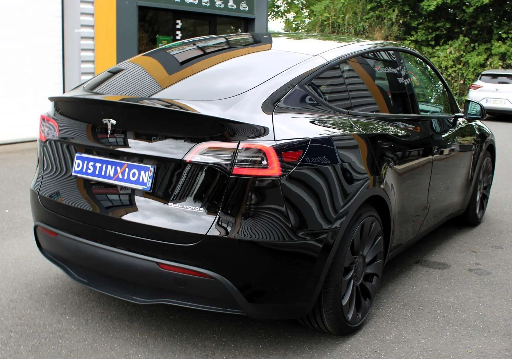 Vue 3/4 arrière droite d'une Tesla Model Y noire métallisée avec jantes noires et logo Tesla visible sur le hayon.