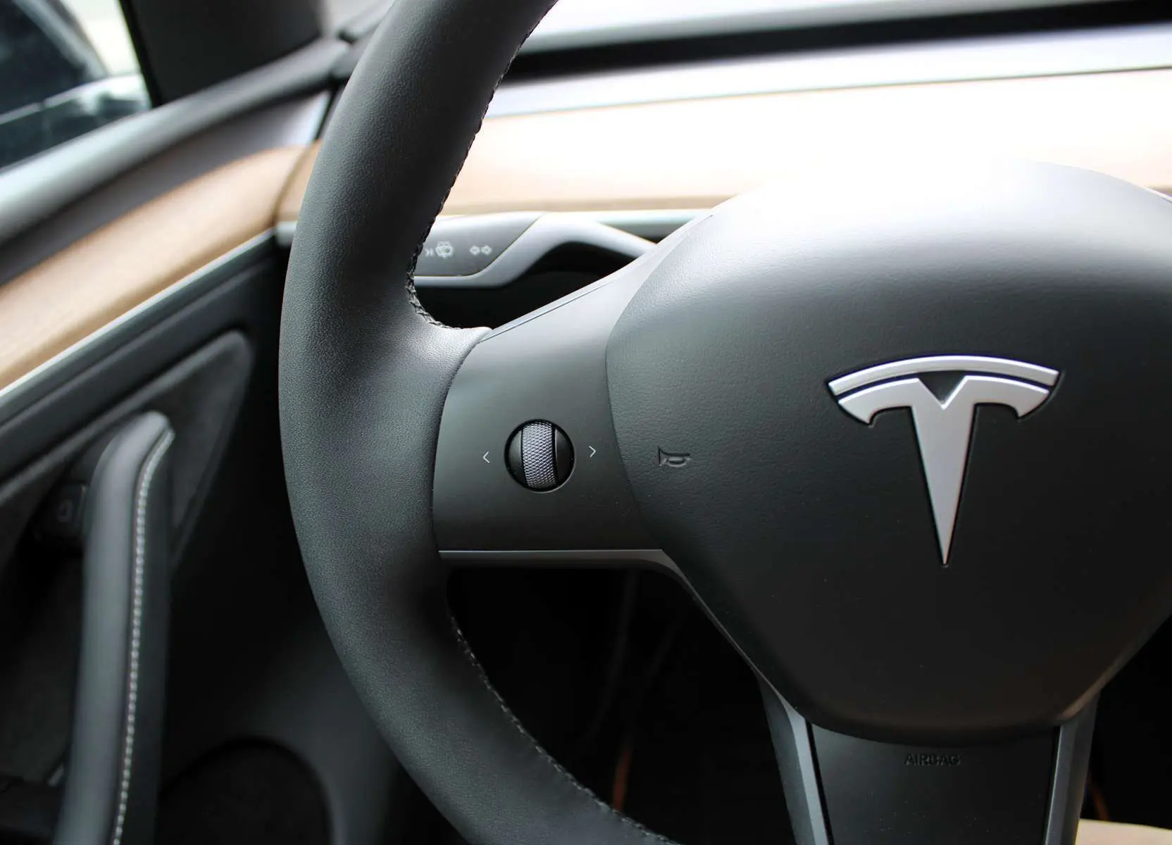 Gros plan sur le volant noir de la Tesla Model Y 2024 avec logo argenté et tableau de bord en bois clair.