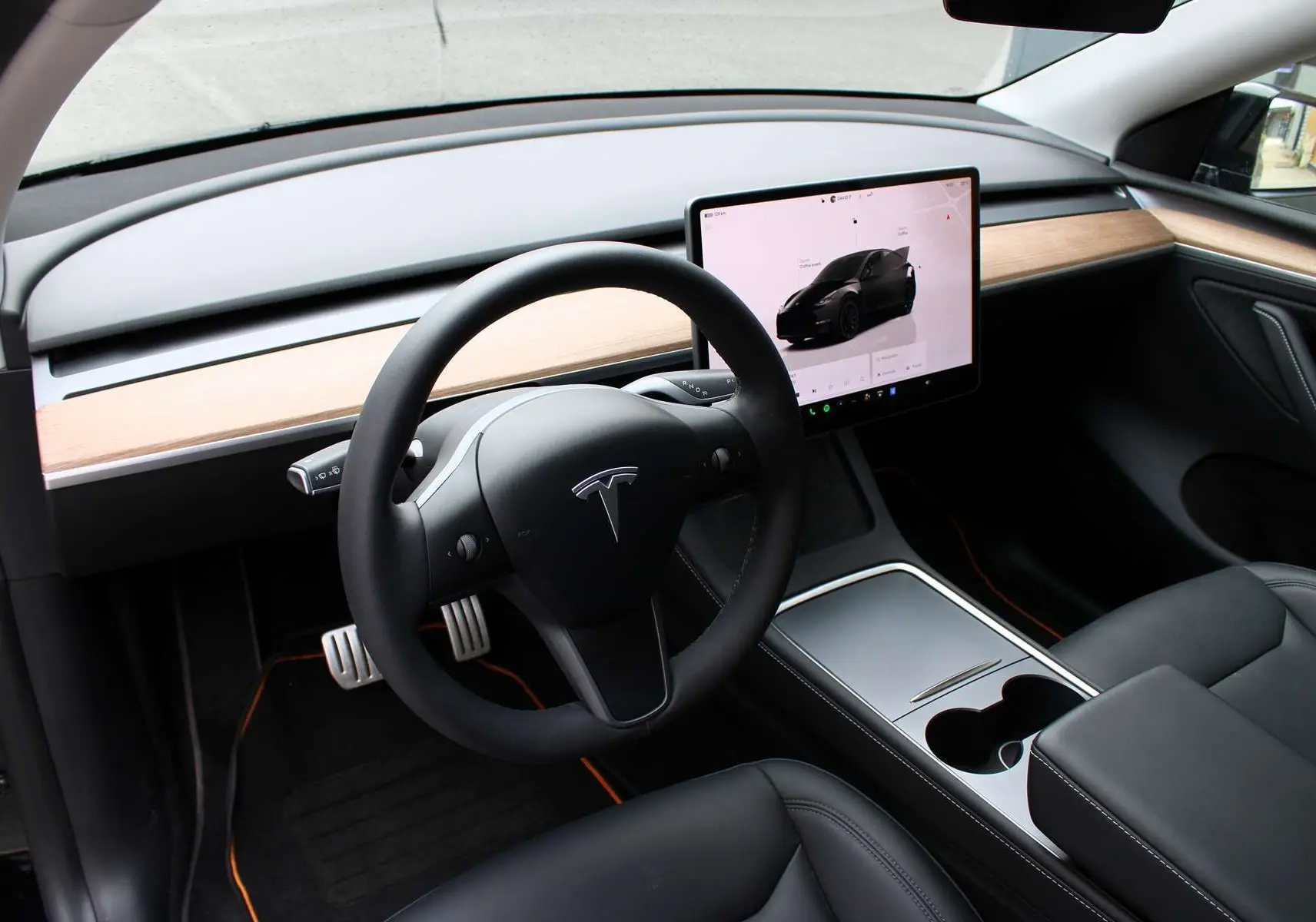 Intérieur de la Tesla Model Y 2024, vue du poste de conduite avec volant noir, écran tactile central et tableau de bord bois clair.