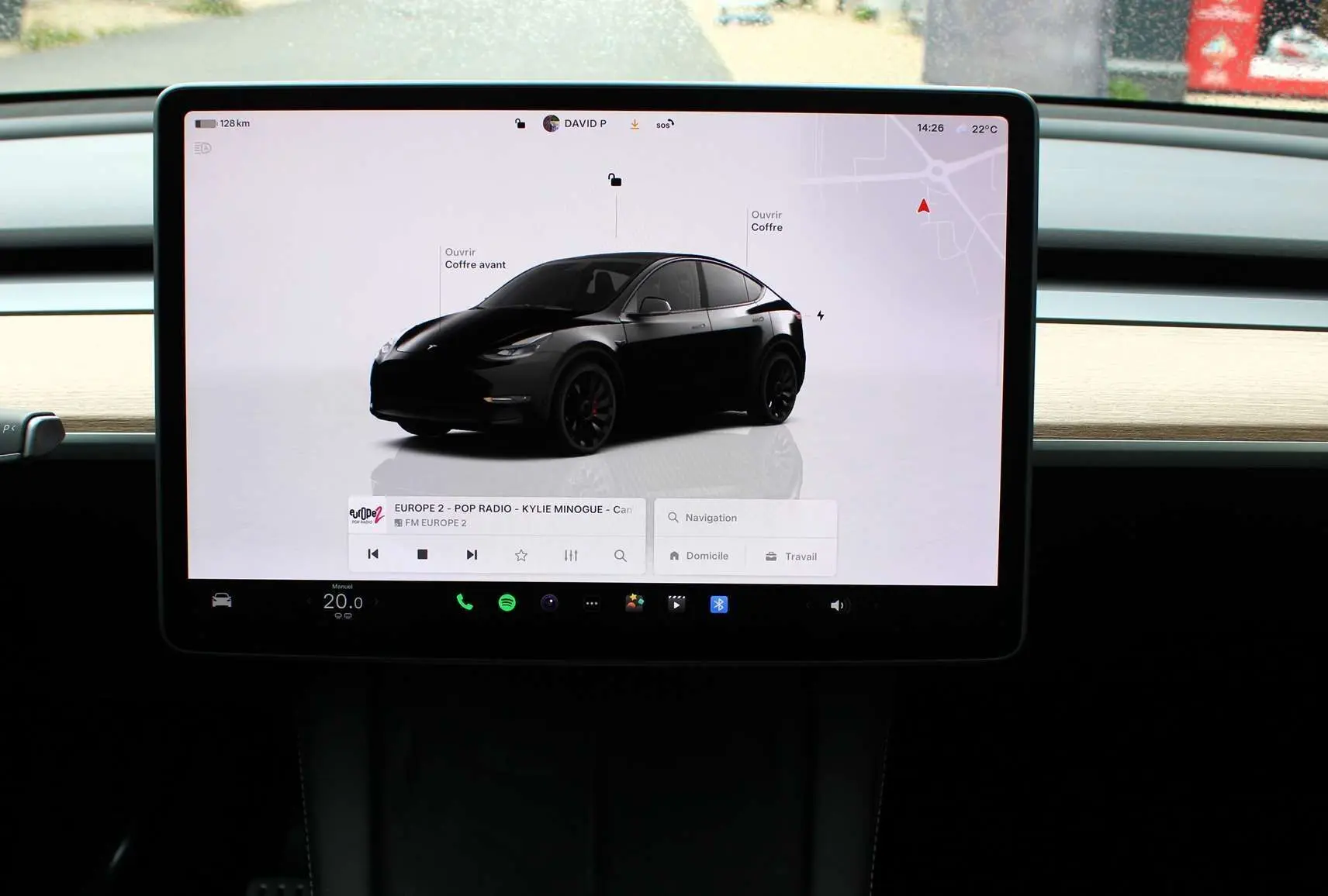 Écran tactile central affichant une Tesla Model Y noir métal en 3/4 avant sur fond blanc, avec options de contrôle visibles.