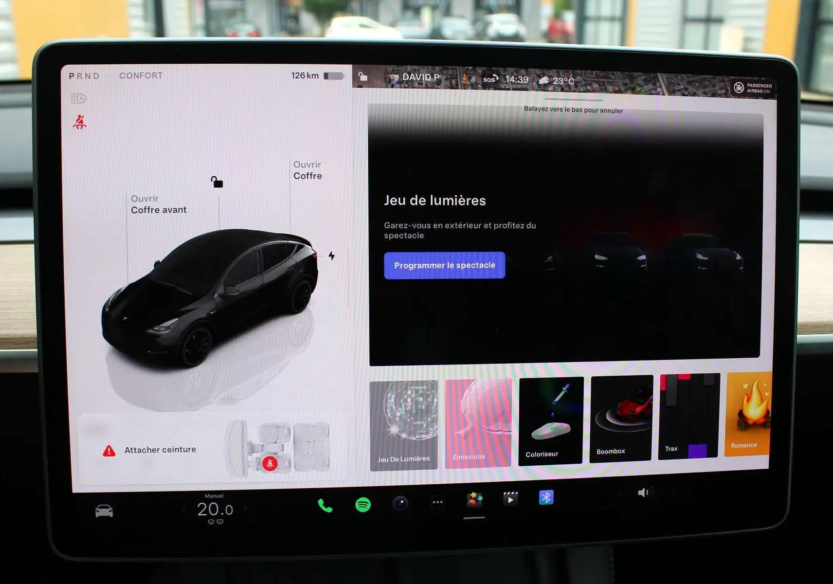 Écran tactile montrant une Tesla Model Y noire métal en vue 3/4 avant avec options d'ouverture des coffres.