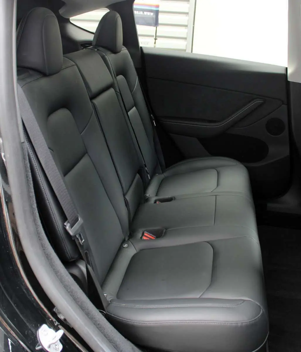 Vue latérale du siège arrière en cuir noir de la Tesla Model Y 2024, avec ceinture de sécurité et porte côté droit visible.