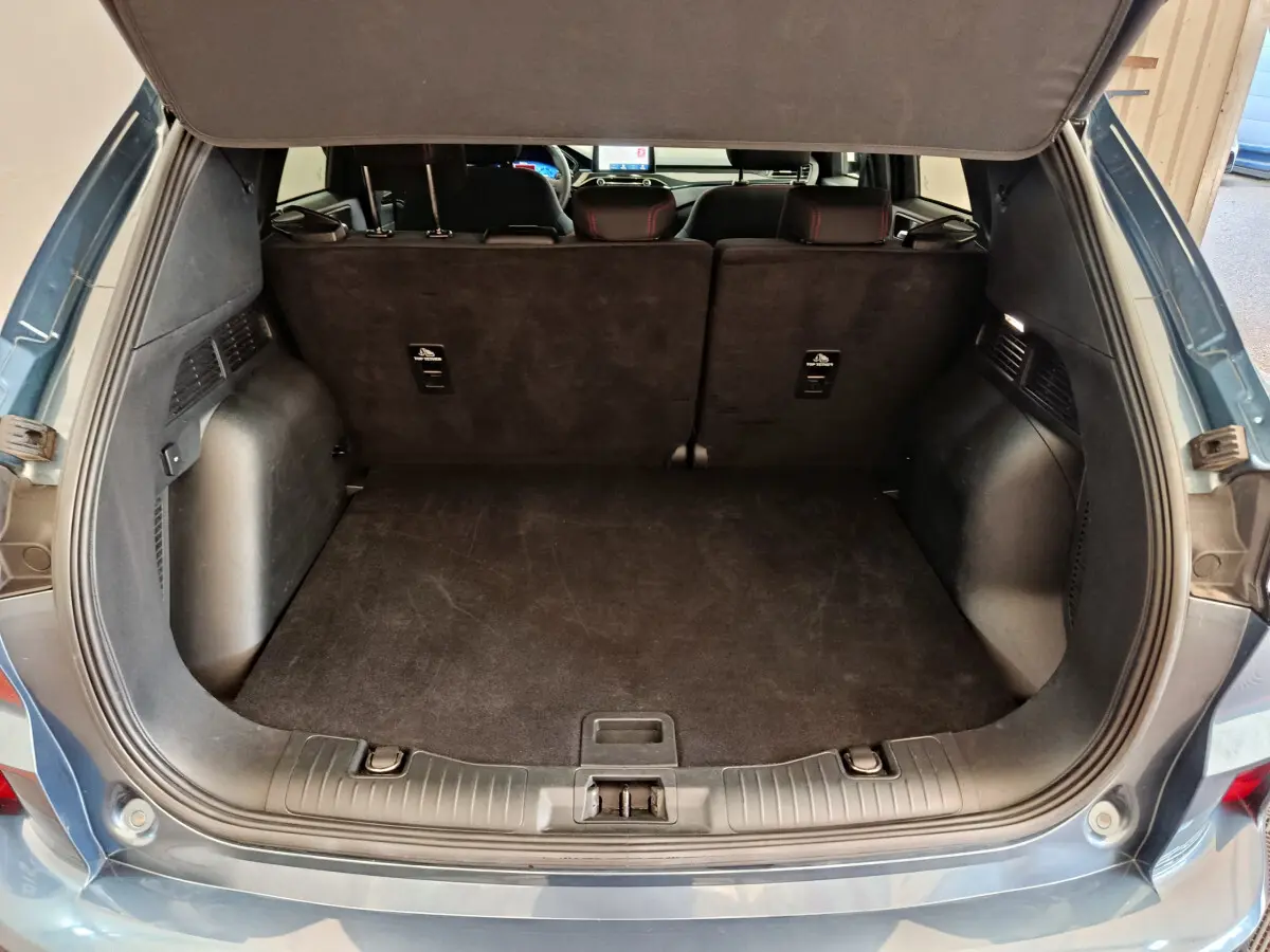 Coffre ouvert d'un Ford Kuga bleu 2024, vue arrière montrant l'espace de chargement et la banquette arrière noire.