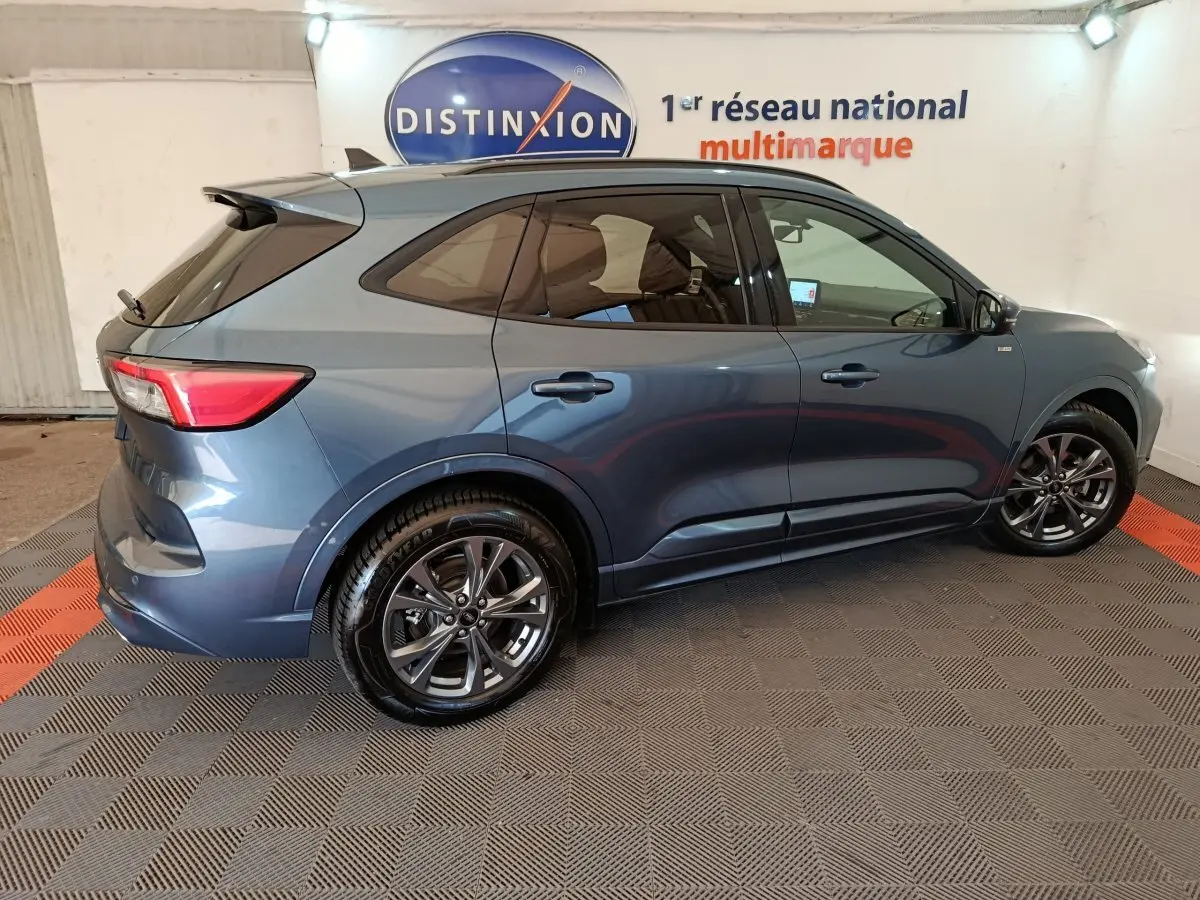 Vue latérale côté gauche d'un Ford Kuga bleu 2024 avec jantes alliage et vitres teintées en intérieur showroom.