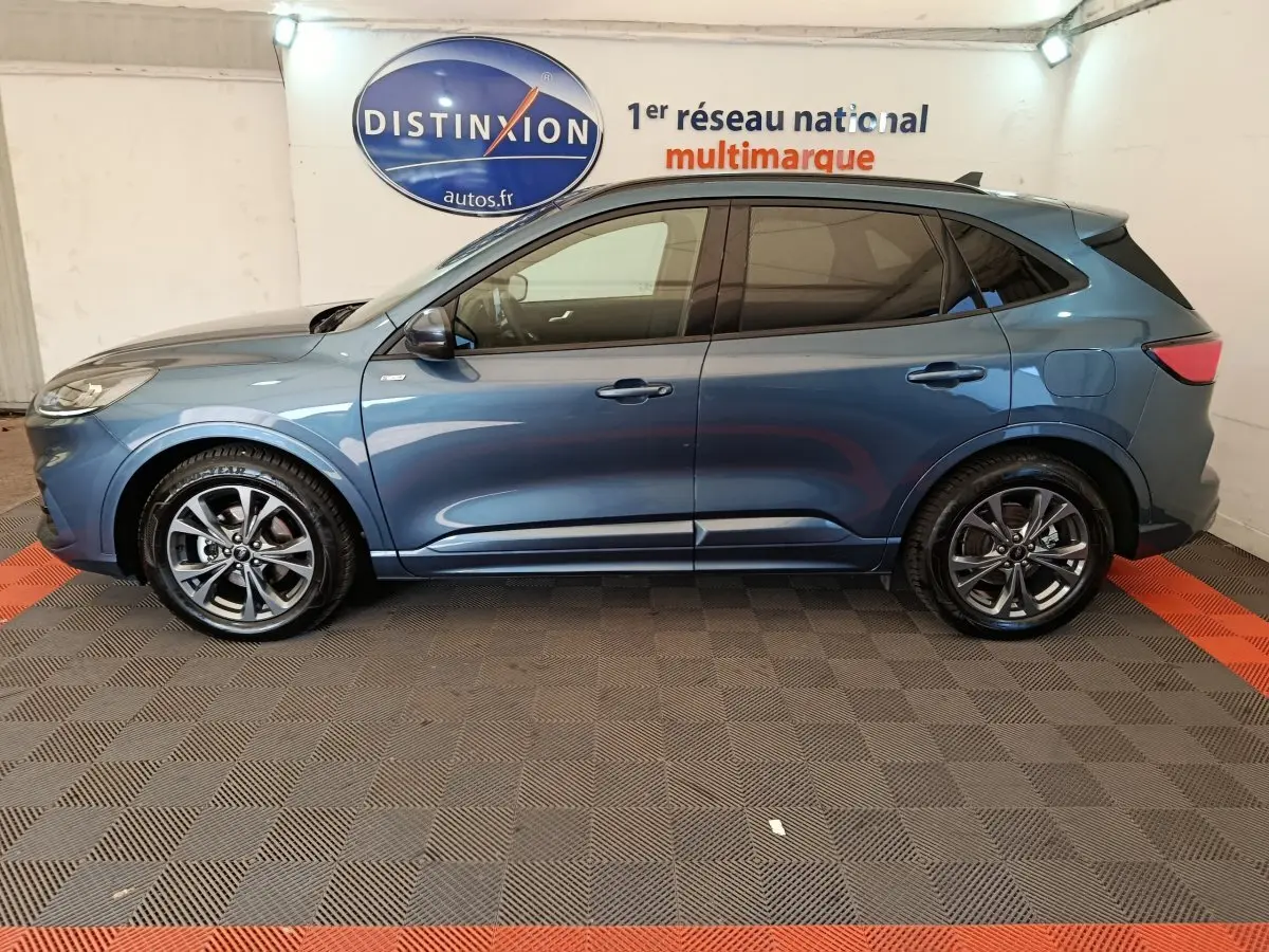 Profil côté gauche du Ford Kuga 2024 bleu St Line avec jantes alliage et vitres teintées en intérieur showroom