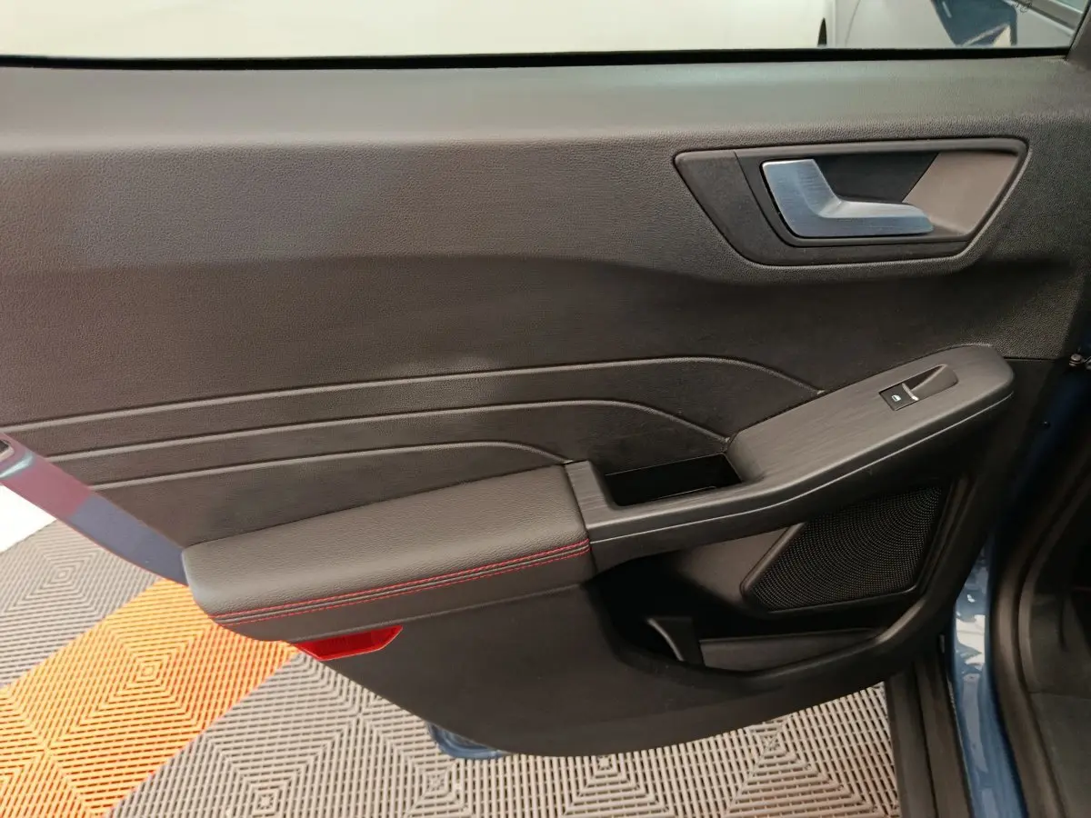Gros plan sur la porte intérieure côté gauche du Ford Kuga bleu, avec surpiqûres rouges et commande de vitre.