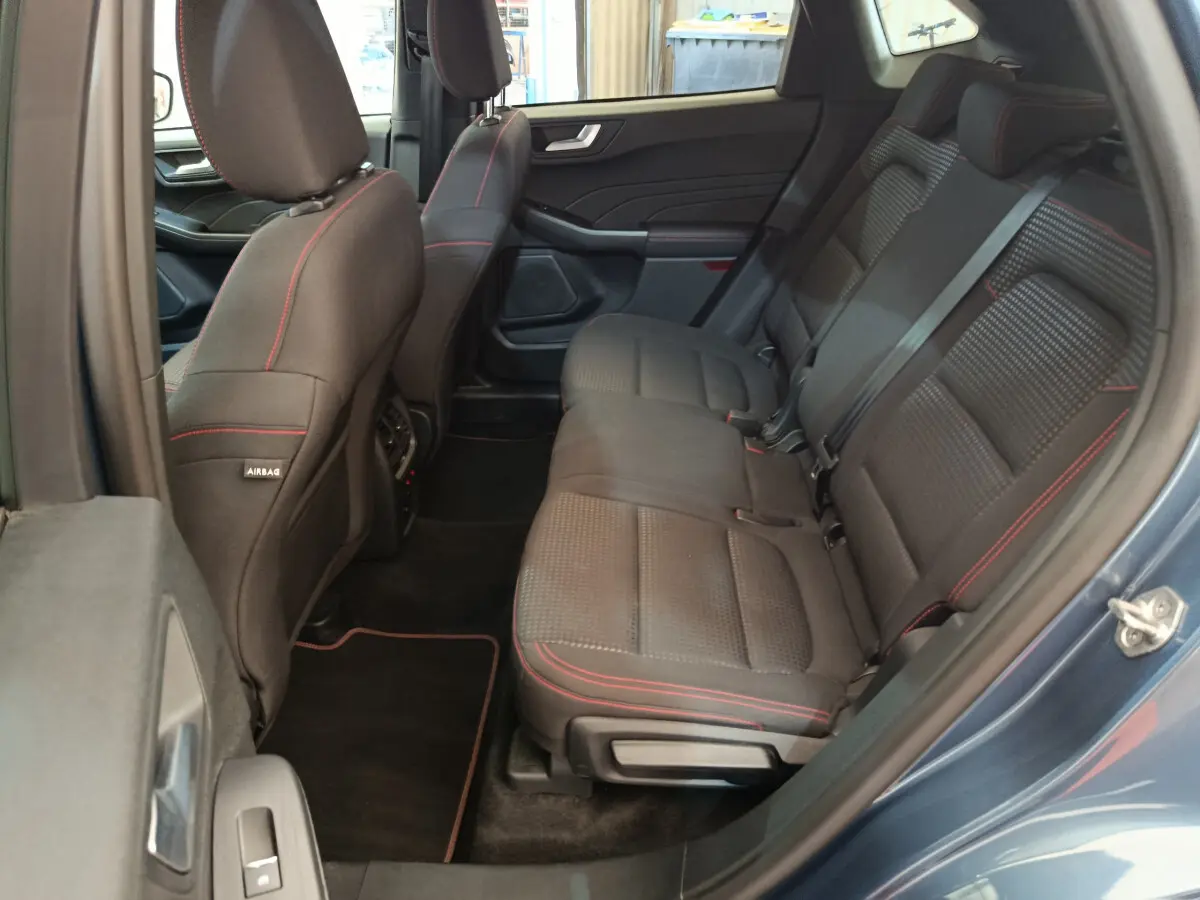 Vue côté droit sur l’intérieur arrière du Ford Kuga bleu 2024, sièges noirs avec surpiqûres rouges et ceintures grises.