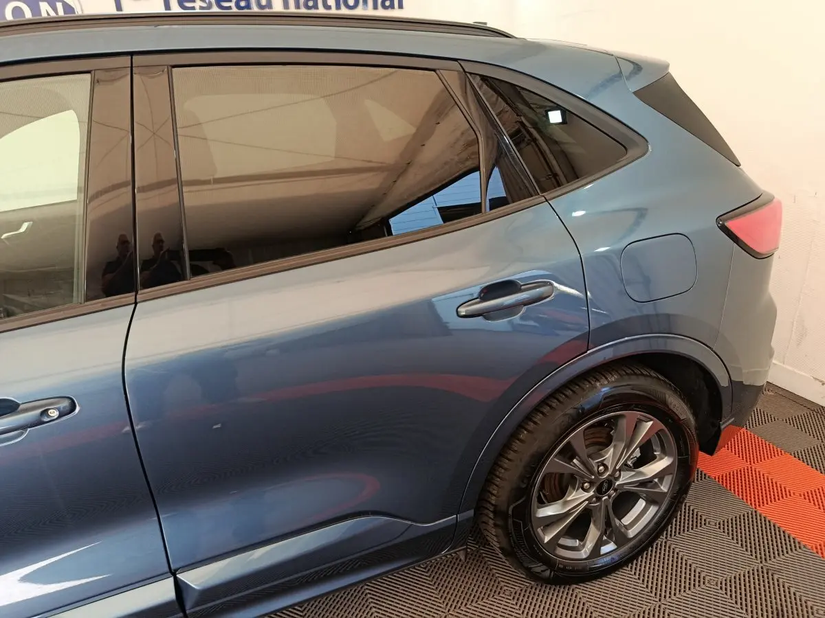 Vue latérale droite du Ford Kuga bleu 2024, mettant en valeur la porte arrière et la roue alliage au design moderne.