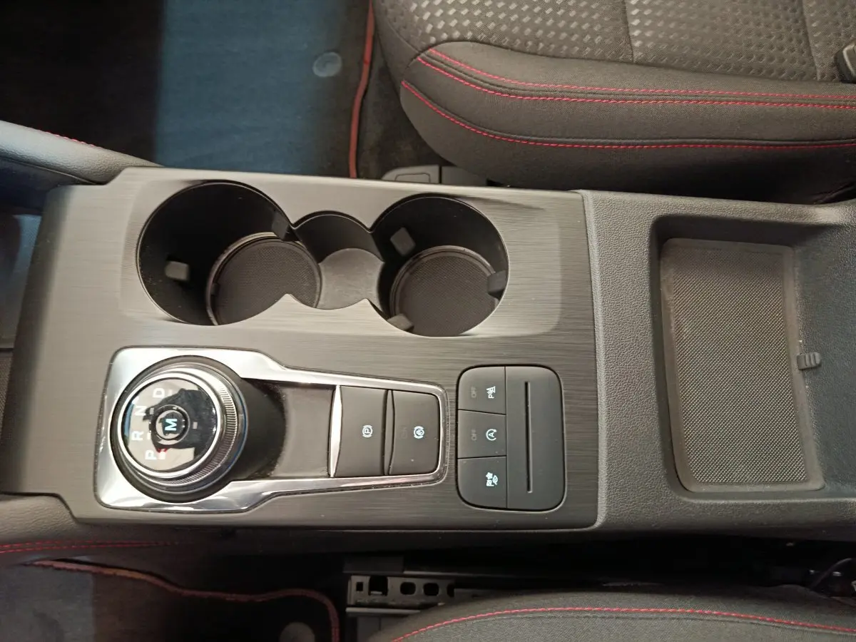 Vue plongeante sur la console centrale noire du Ford Kuga bleu 2024 avec molette de boîte auto et surpiqûres rouges.