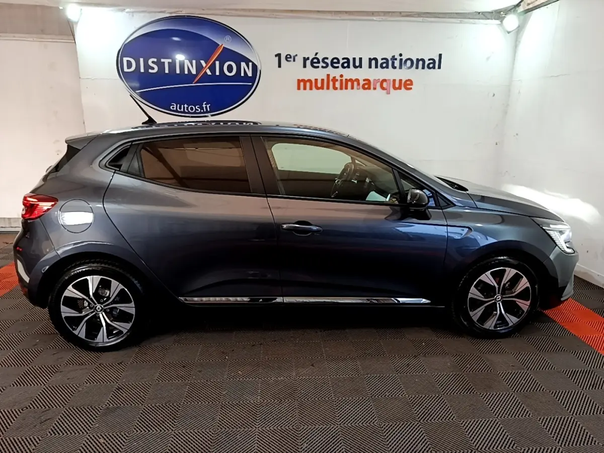 Profil droit d'une Renault Clio Evolution SCe 65 gris foncé 2022 avec jantes alliage et vitres teintées en intérieur showroom.