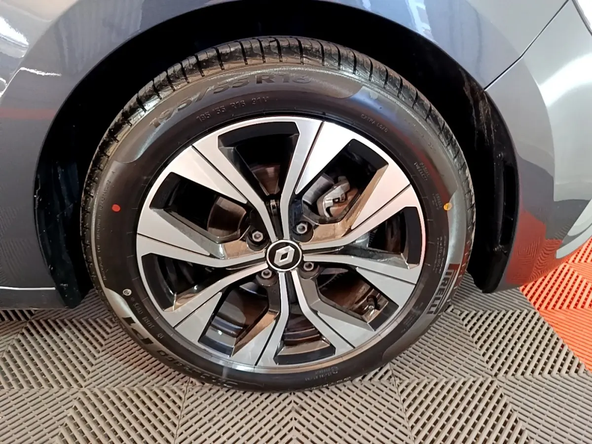 Gros plan sur la roue avant gauche d'une Renault Clio gris foncé, mettant en valeur la jante alliage au design moderne.