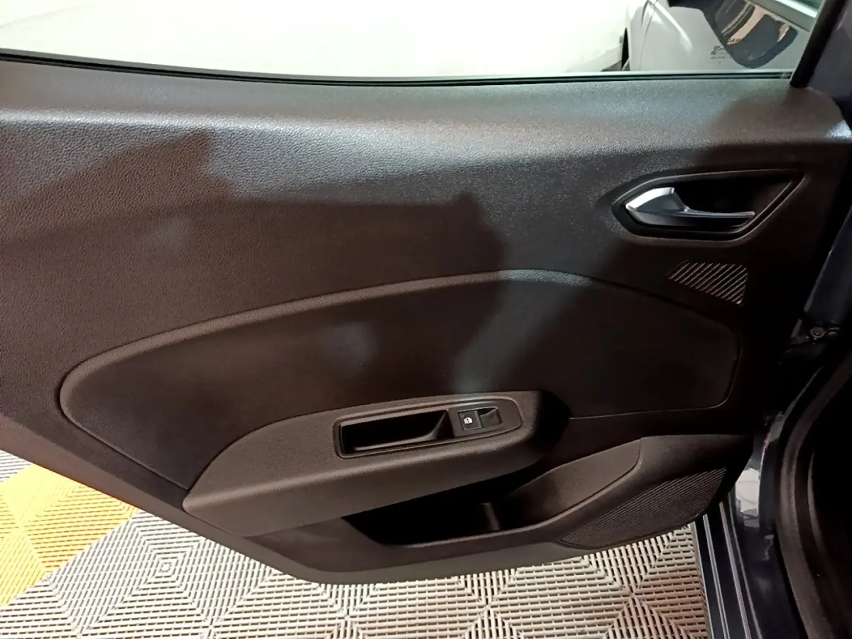 Gros plan sur la porte intérieure côté arrière droit de la Renault Clio gris foncé, avec poignée et commande de vitre.