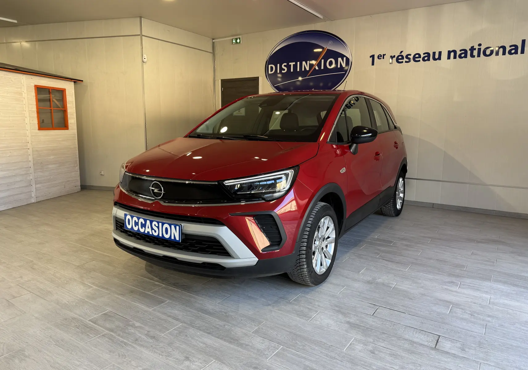 Vue 3/4 avant d’un Opel Crossland rouge 2022 en intérieur, avec calandre noire et plaque « OCCASION » visible.