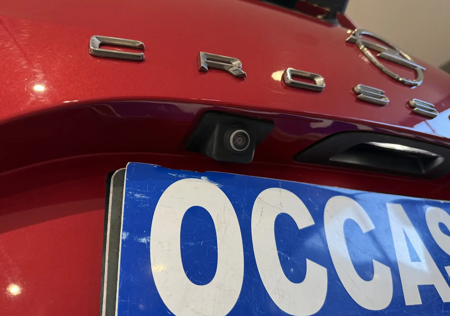 Gros plan sur la caméra de recul et le logo Opel Crossland rouge à l'arrière du véhicule, avec plaque d'immatriculation partielle.