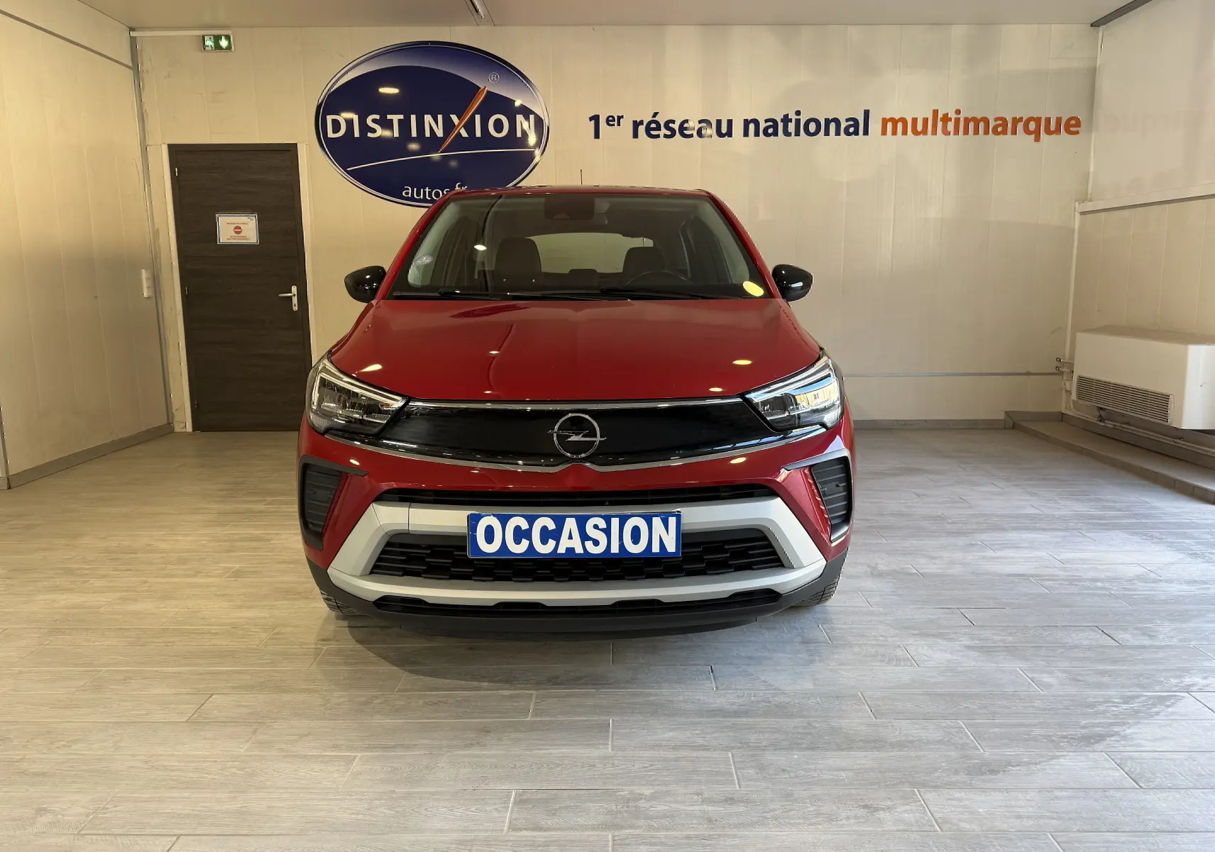 Vue frontale d'un Opel Crossland rouge 2022 avec calandre noire et plaque "OCCASION" en intérieur showroom.