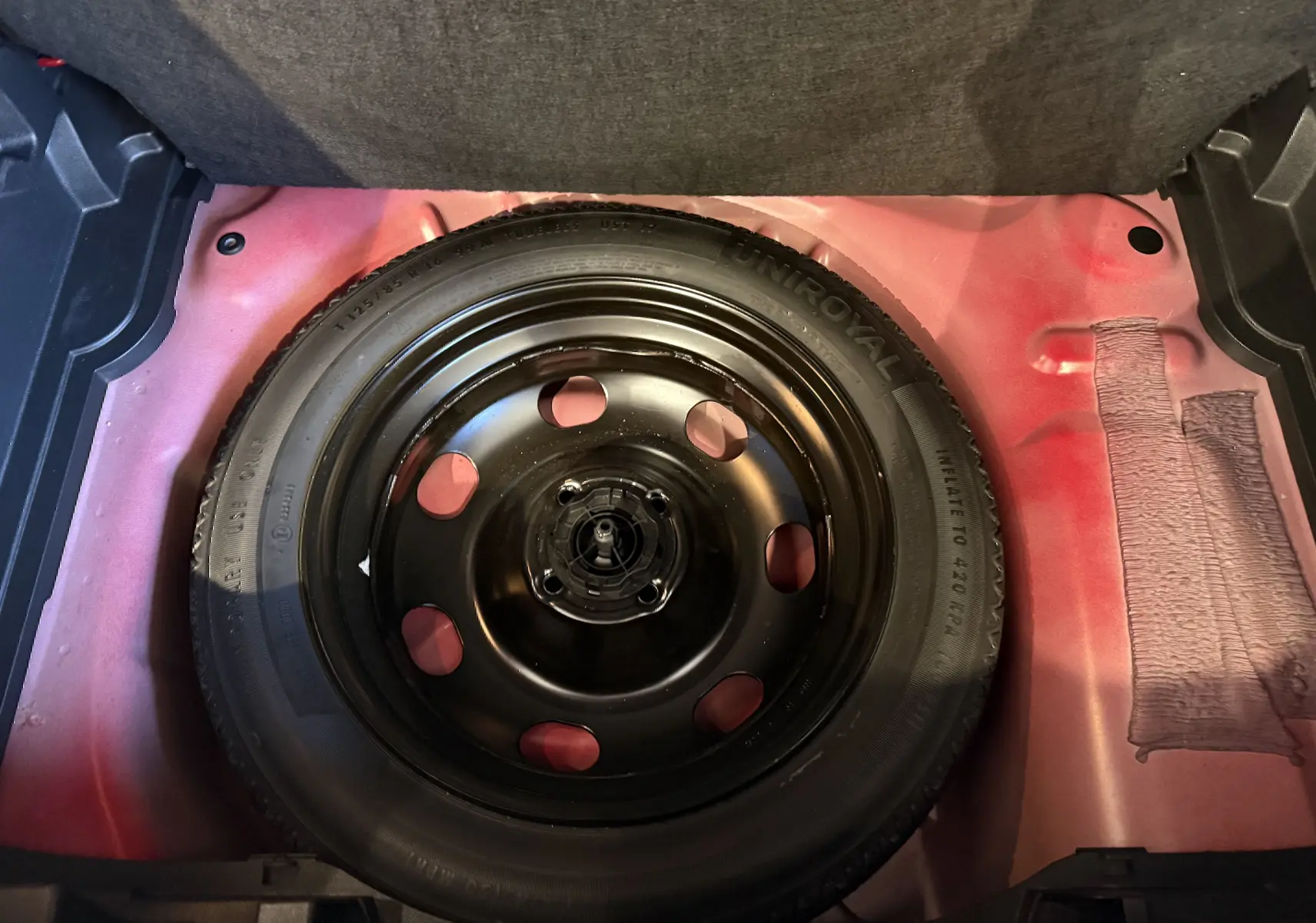 Vue plongeante sur la roue de secours noire dans le coffre rouge de l’Opel Crossland 2022 finition Elegance Business.