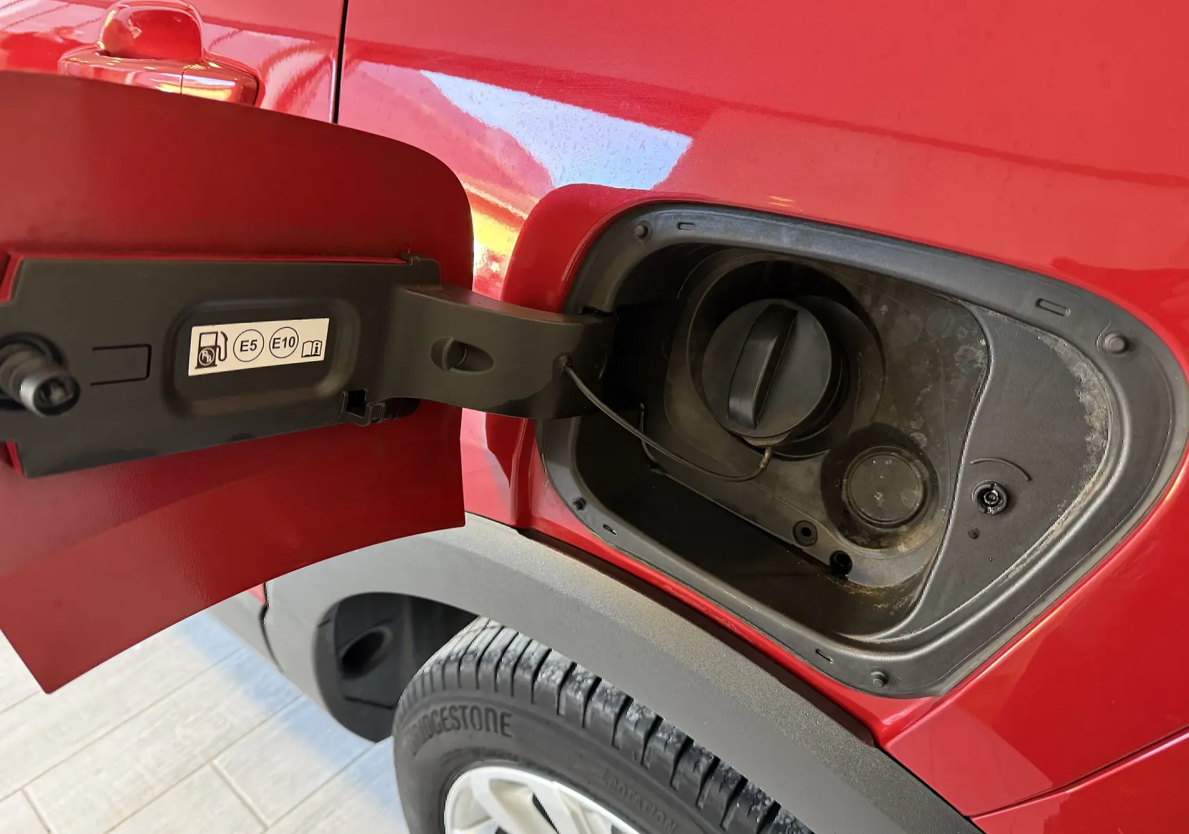 Vue rapprochée de la trappe à carburant ouverte côté gauche d’un Opel Crossland rouge avec pneu Bridgestone visible.