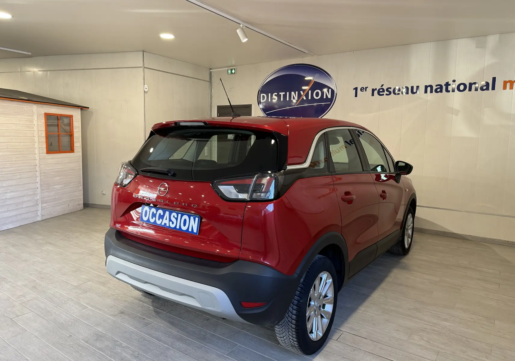 Vue 3/4 arrière droite d’un Opel Crossland rouge 2022 en intérieur, avec détails noirs contrastants et plaque "OCCASION".