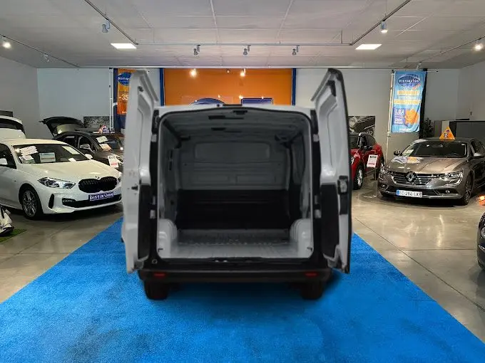 Vue arrière du Renault Trafic Fourgon blanc avec portes arrière ouvertes montrant l’espace de chargement vide dans un showroom.
