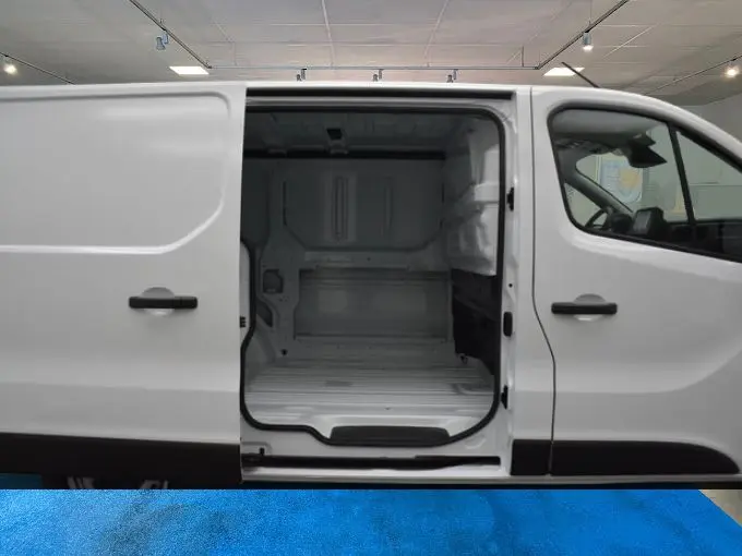 Vue latérale droite d’un Renault Trafic Fourgon blanc L1H1 avec porte coulissante ouverte montrant l’espace de chargement vide.