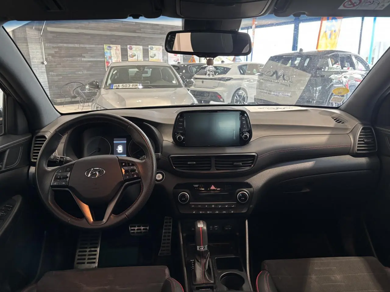 Vue intérieure avant du Hyundai Tucson noir 2020, tableau de bord et volant sport N Line avec surpiqûres rouges.