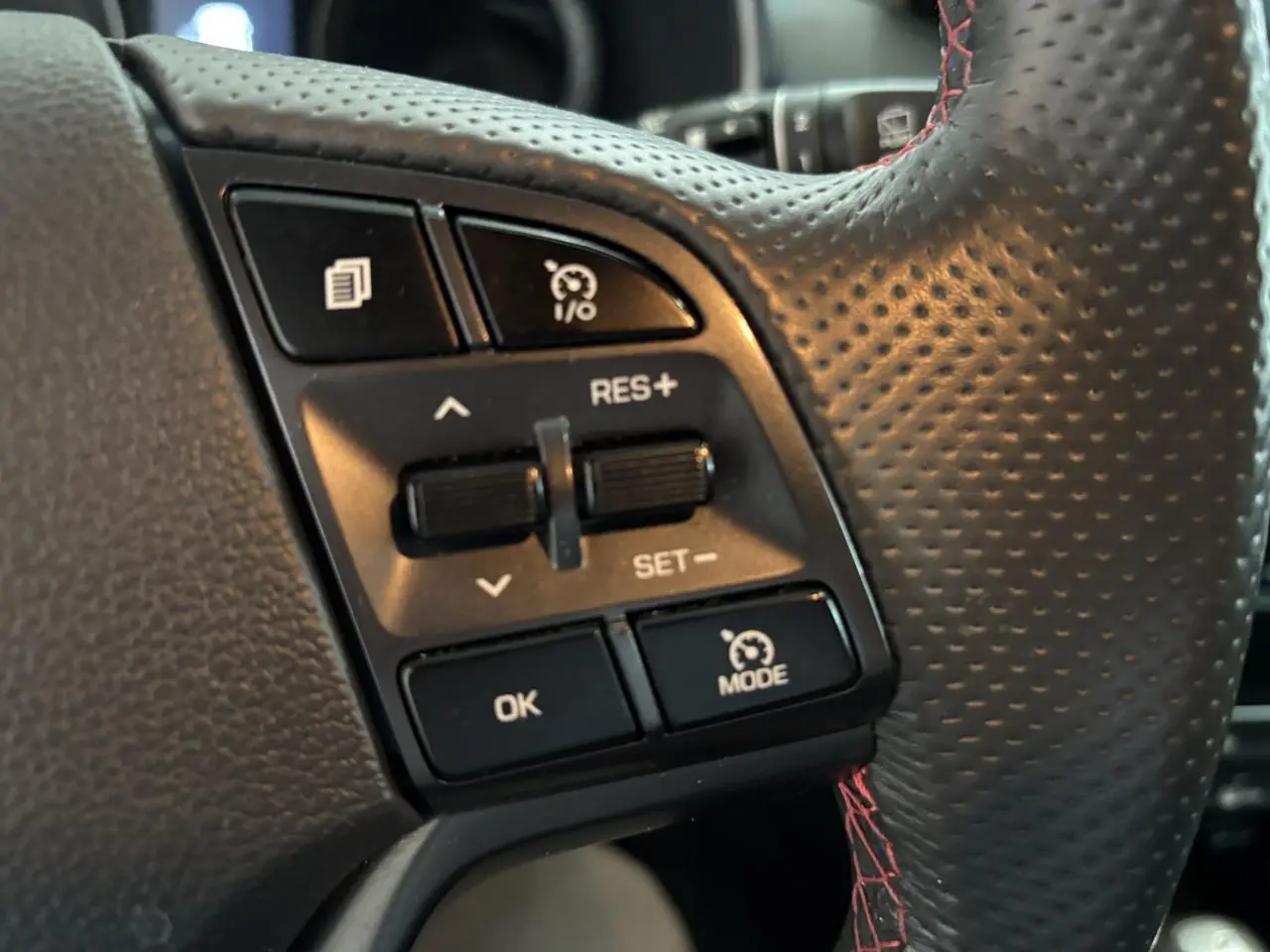 Gros plan sur les commandes de régulateur de vitesse du volant cuir noir perforé avec surpiqûres rouges du Hyundai Tucson N Line.